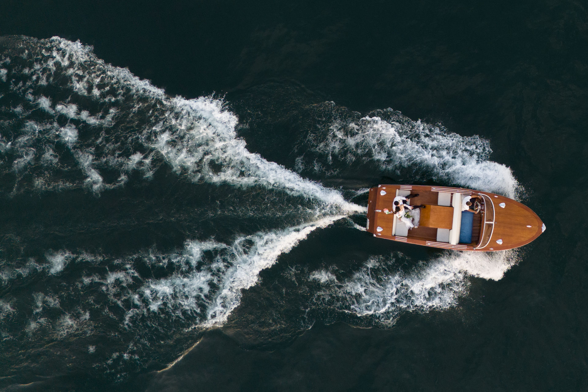 A wooden motorboat is travelling through the dark water, leaving a white trail of foam behind it.