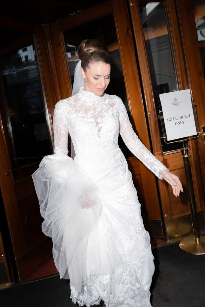 Eine Braut im Spitzenhochzeitskleid verlässt ein Gebäude mit ihrem Kleid und Schleier in der Hand in der Nähe eines Schildes "Hotel Guest Only".