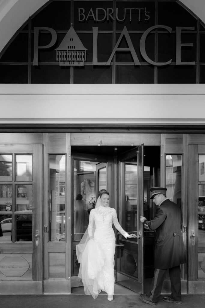 Eine Braut in einem Spitzenkleid verlässt den Badrutt's Palace, während ein Pförtner ihr die Tür aufhält.