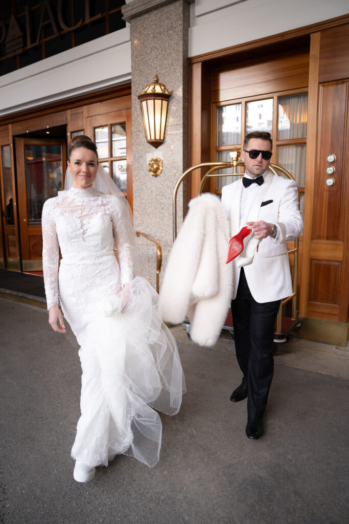 Eine Braut in einem weißen Kleid und ein Mann im Smoking stehen vor einem Gebäude; er hält ihren weißen Pelzmantel. Heiraten in der Schweiz