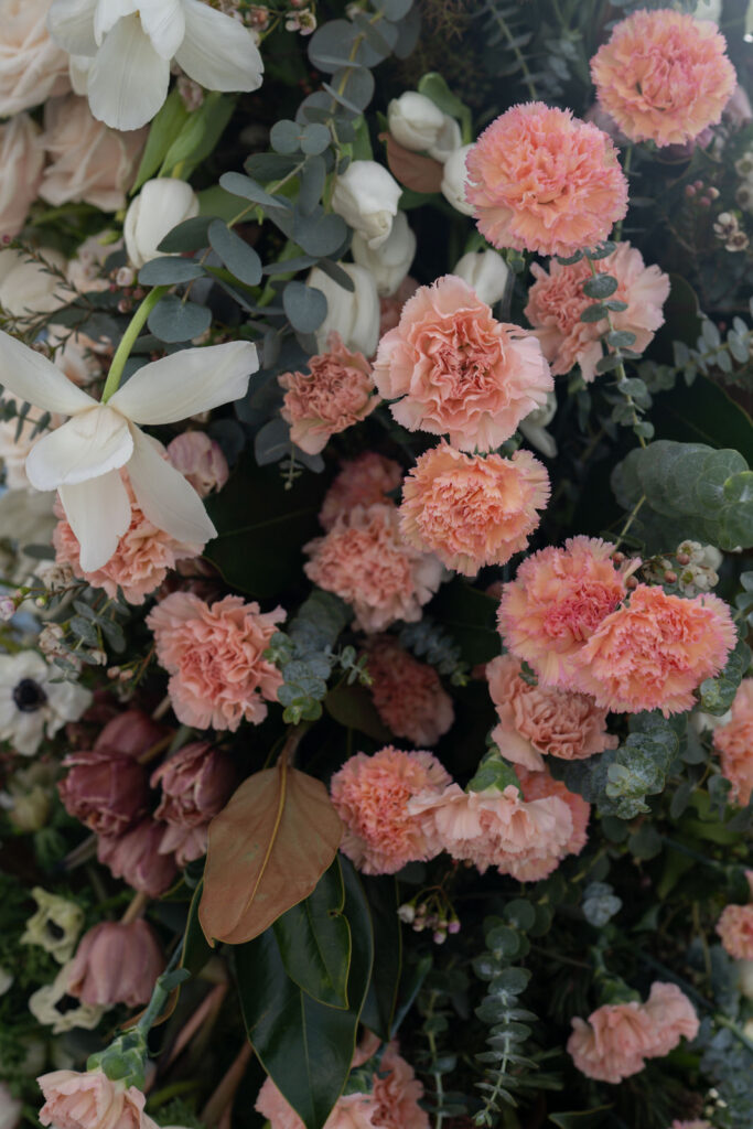 Cluster aus pfirsichfarbenen Nelken, weißen Tulpen und Eukalyptusblättern, arrangiert in einem üppigen Blumenstrauß.