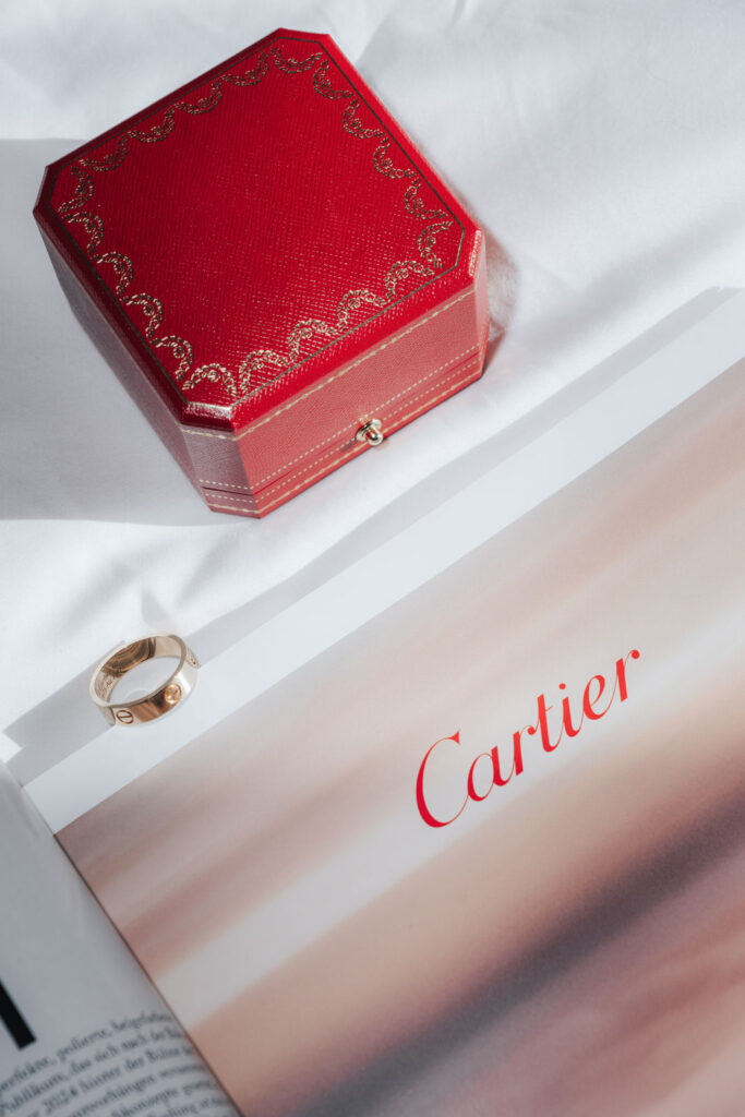 Ein goldener Ring, eine rote Cartier-Schachtel und das Cartier-Logo auf einer Magazinseite auf einer weißen Fläche.