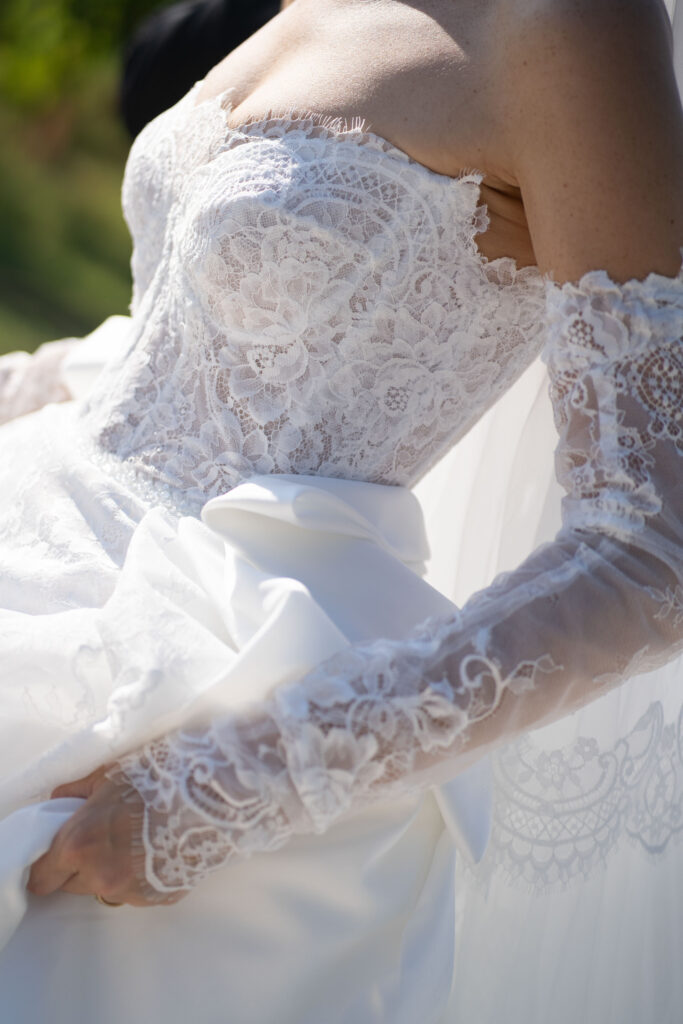 Conti di San Bonifacio Wine Resort: Exklusive Hochzeit in der Toskana, Italien 82 Eine Nahaufnahme einer Braut in einem schulterfreien Spitzenhochzeitskleid, die ihr weißes Kleid hält, aufgenommen von einer Hochzeitsfotografin, die sich auf Hochzeitsfotografie im Ausland spezialisiert hat.