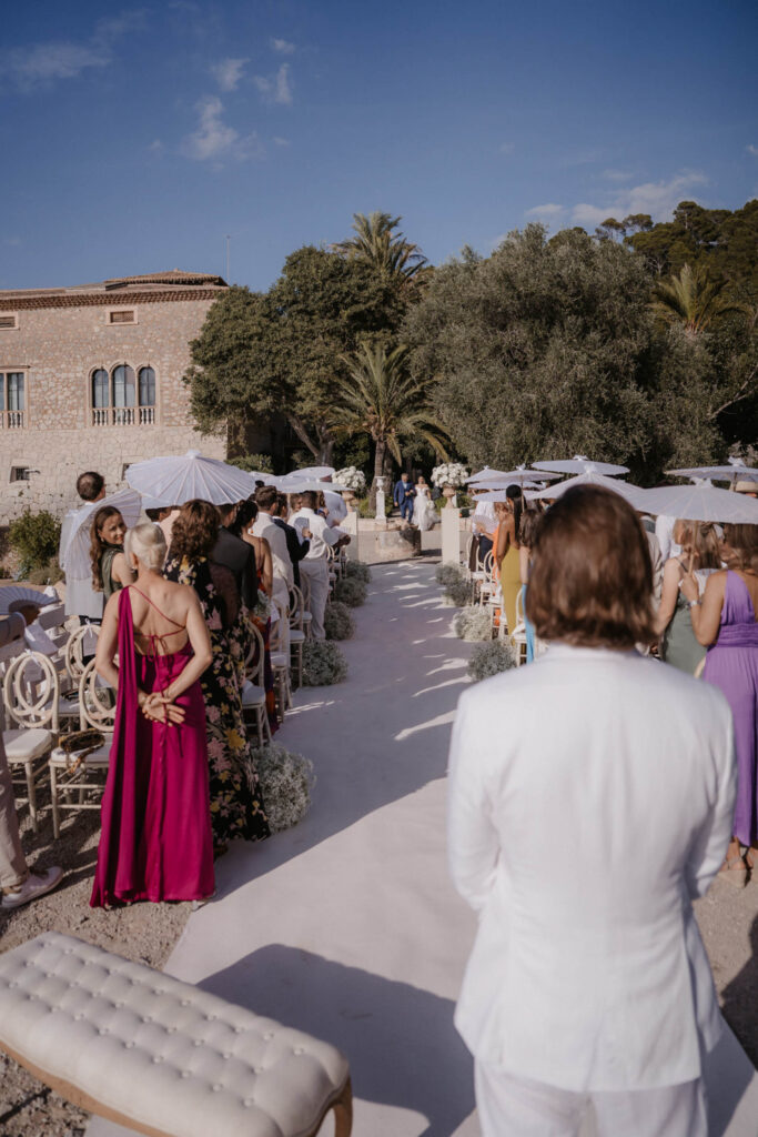 Braut und Bräutigam schreiten in Son Marroig den Gang entlang, während die Gäste ihrer Hochzeit im Freien beiwohnen.
