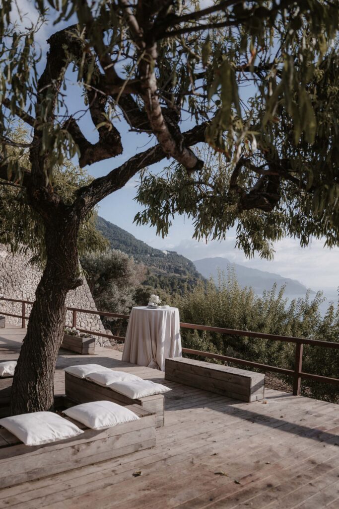 Ein kleiner Tisch und Holzbänke mit Kissen auf einer Terrasse in Son Marroig mit Blick auf das Meer.