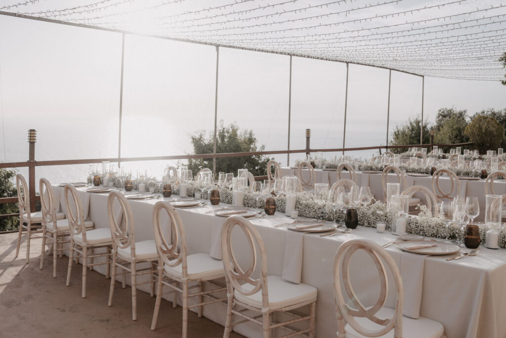 Hochzeitstisch im Long Son Marroig mit weißen Stühlen und Blumengestecken mit Blick auf das Meer.