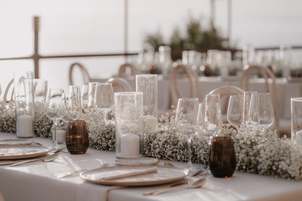 Eine Tischdekoration für eine Hochzeit in Son Marroig mit Schleifen aus Schleierkraut, Stumpenkerzen und Glasgeschirr.