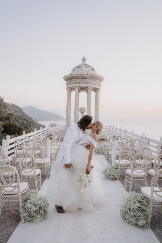 Ein frisch verheiratetes Paar küsst sich in Son Marroig, einer Hochzeitslocation im Freien mit Blick auf das Meer.