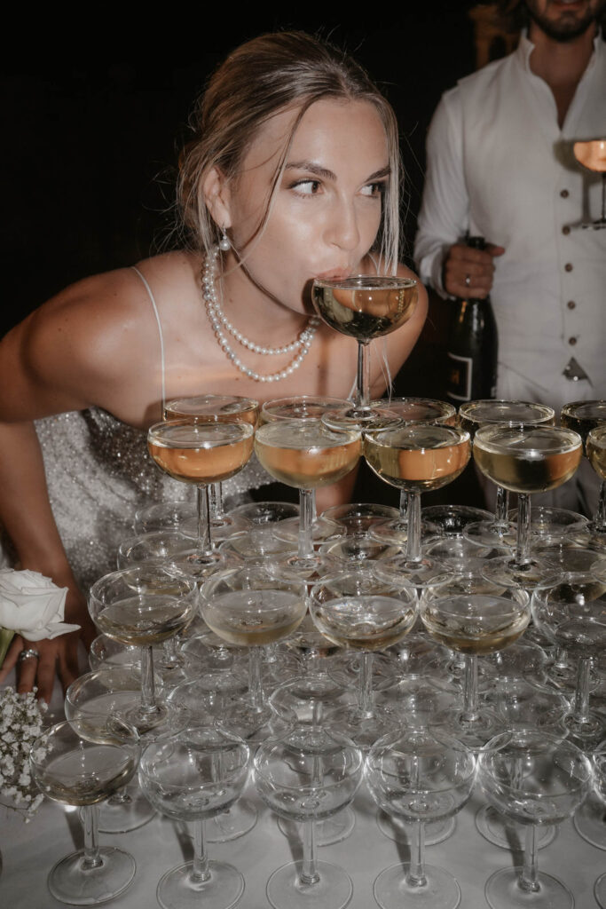 Wedding in Son Marroig: Getting married over the cliffs of Mallorca, with experience, costs and tips 17 A woman in a beaded dress is sipping from a glass that stands at the very top of a Son-Marroig champagne tower.