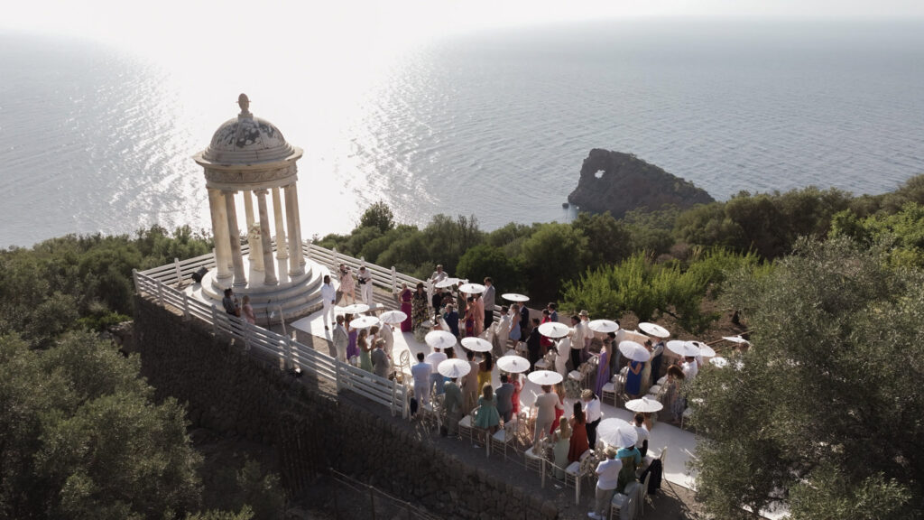 Wedding in Son Marroig: Getting married over the cliffs of Mallorca, with experience, costs and tips 6 Wedding guests with white umbrellas gathered for a ceremony in the Rotunda of Son Marroig by the sea.
