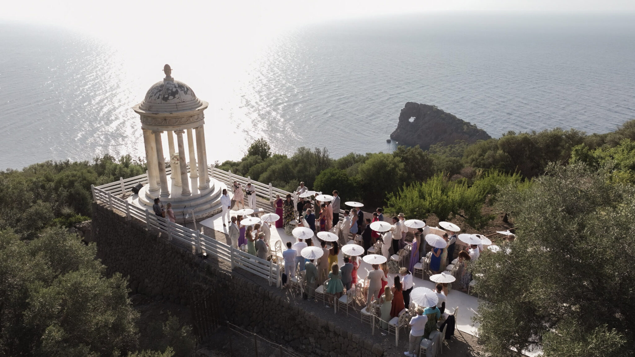 Hochzeitsgäste mit weißen Sonnenschirmen versammelten sich zu einer Zeremonie in der Rotunde von Son Marroig am Meer.