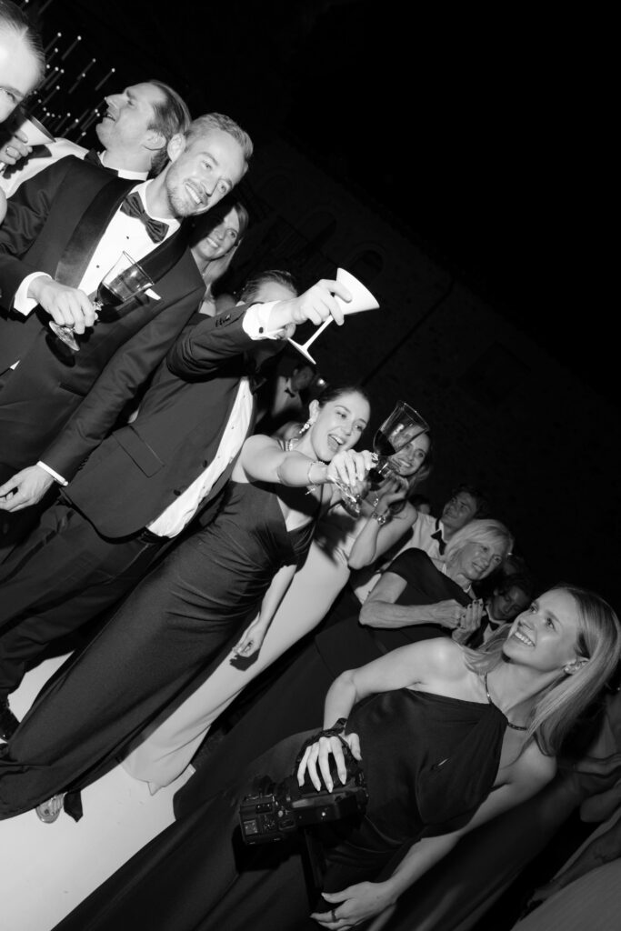 A group of formally dressed people, smiling and raising their glasses in a toast to a wedding abroad, captures the joy of destination wedding photography.