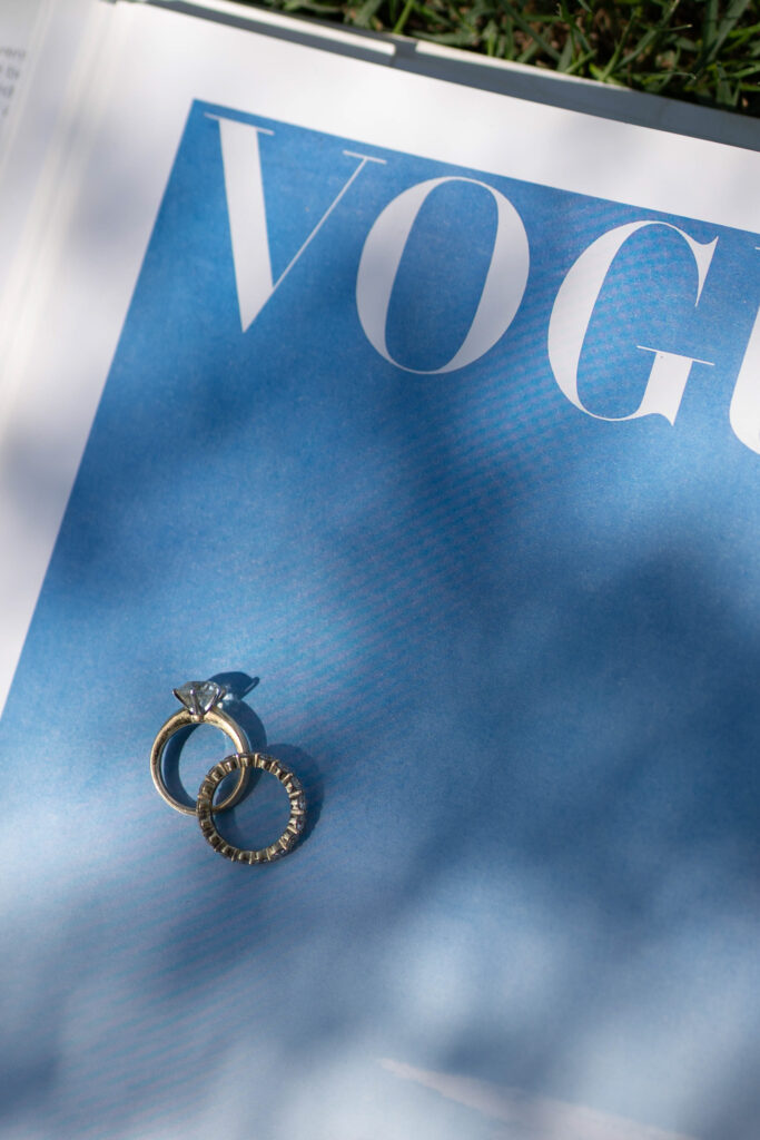 Two rings rest on a Vogue magazine page with a blue background and partial grass shadows - an elegant scene, perfect for wedding photography or any destination wedding.
