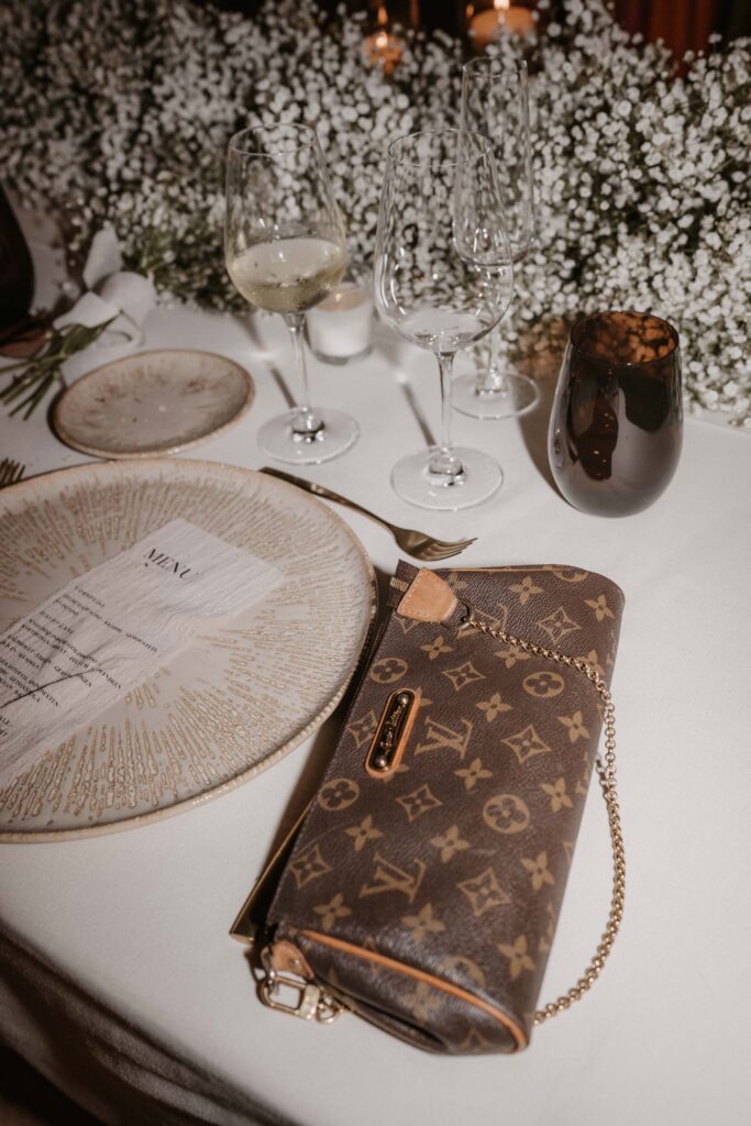 Wedding in Son Marroig: Getting married over the cliffs of Mallorca, with experience, costs and tips 33 A Louis Vuitton clutch on a table with plates, glasses, a menu, and fern flowers – the perfect inspiration for weddings abroad and destination weddings.