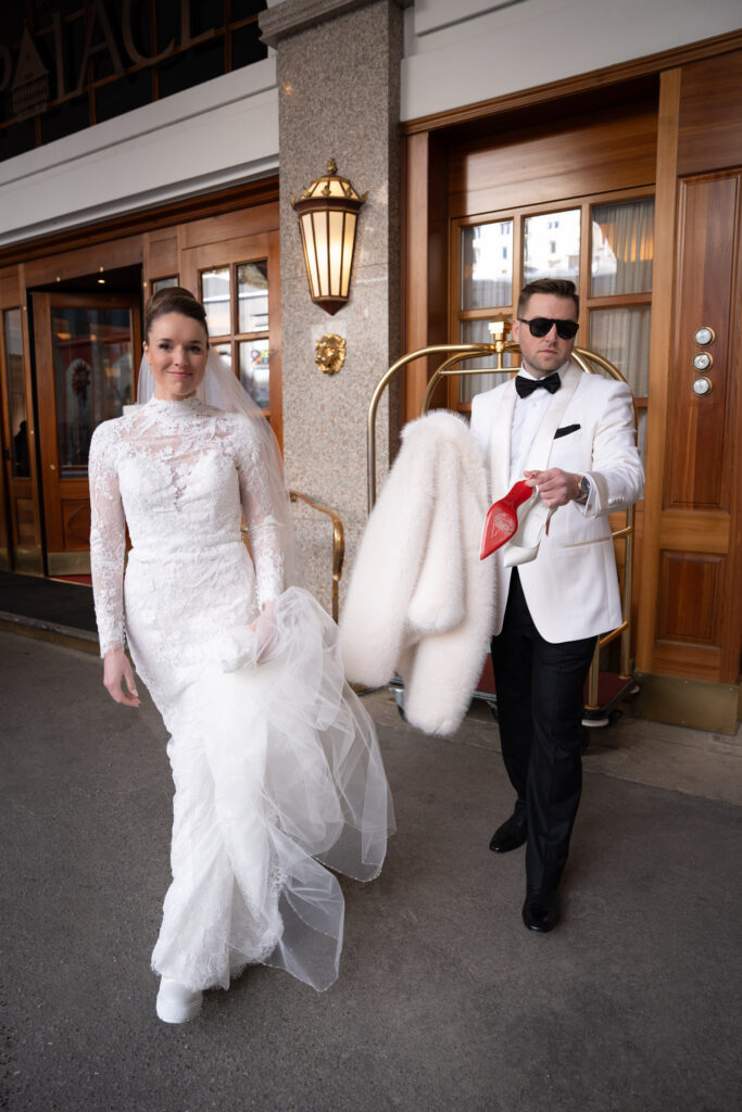 Bride in a white wedding dress and groom in a tuxedo standing in front of a building; the groom is holding a coat - taken by a wedding photographer, perfect for inspiration for your own destination wedding.