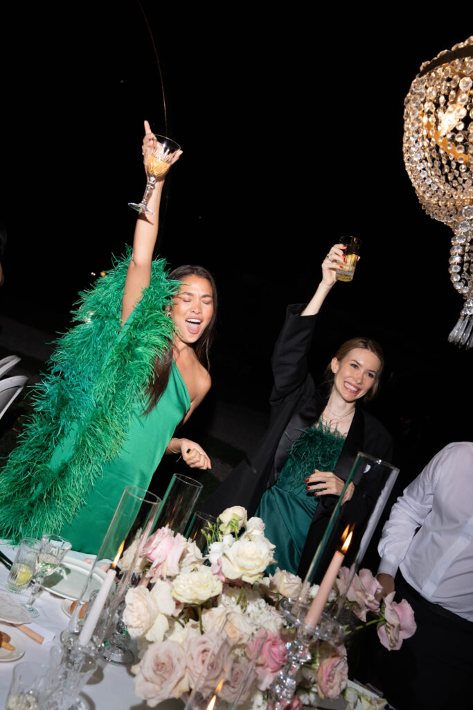 Heiraten am Gardasee: Locations, Kosten und ehrliche Erfahrungen aus über 15 Hochzeiten 8 Zwei Frauen in grünen Kleidern feiern auf einer schicken Dinnerparty in Italien bei Kerzenschein, heben die Gläser und lächeln - und fangen so die Freude und Eleganz einer Hochzeit am Urlaubsort ein.