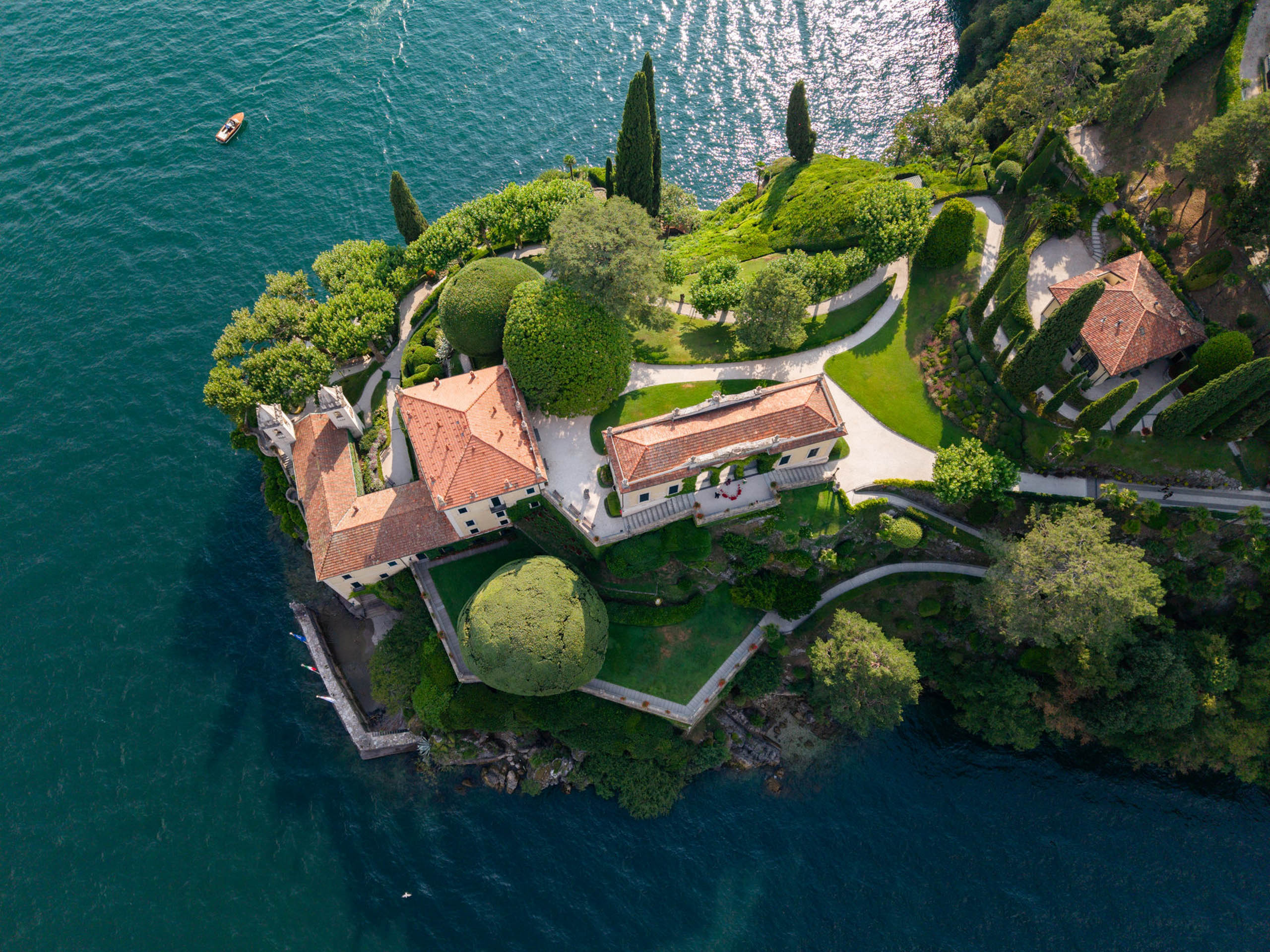 Villa del Balbianello Hochzeit: Kosten, Ablauf und die ikonischste Location am Comer See 57 Aerial view of Villa del Balbianello with its orange-colored roofs on a wooded peninsula in a lake.