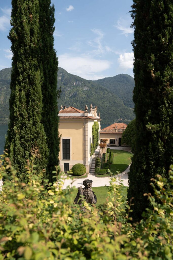 Villa del Balbianello Hochzeit: Kosten, Ablauf und die ikonischste Location am Comer See 15 The Villa del Balbianello, a yellow villa on a lake, surrounded by cypresses and overlooking the mountains in the distance.