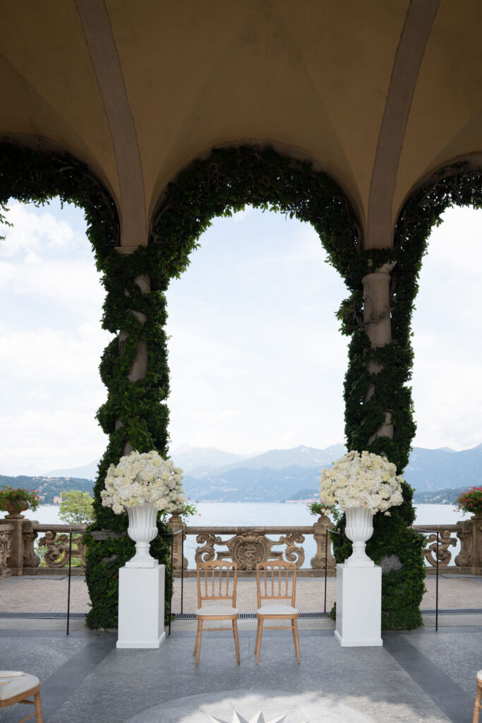 Villa del Balbianello Hochzeit: Kosten, Ablauf und die ikonischste Location am Comer See 19 Between the flower arrangements are two wooden chairs under a stone arch at Villa del Balbianello.