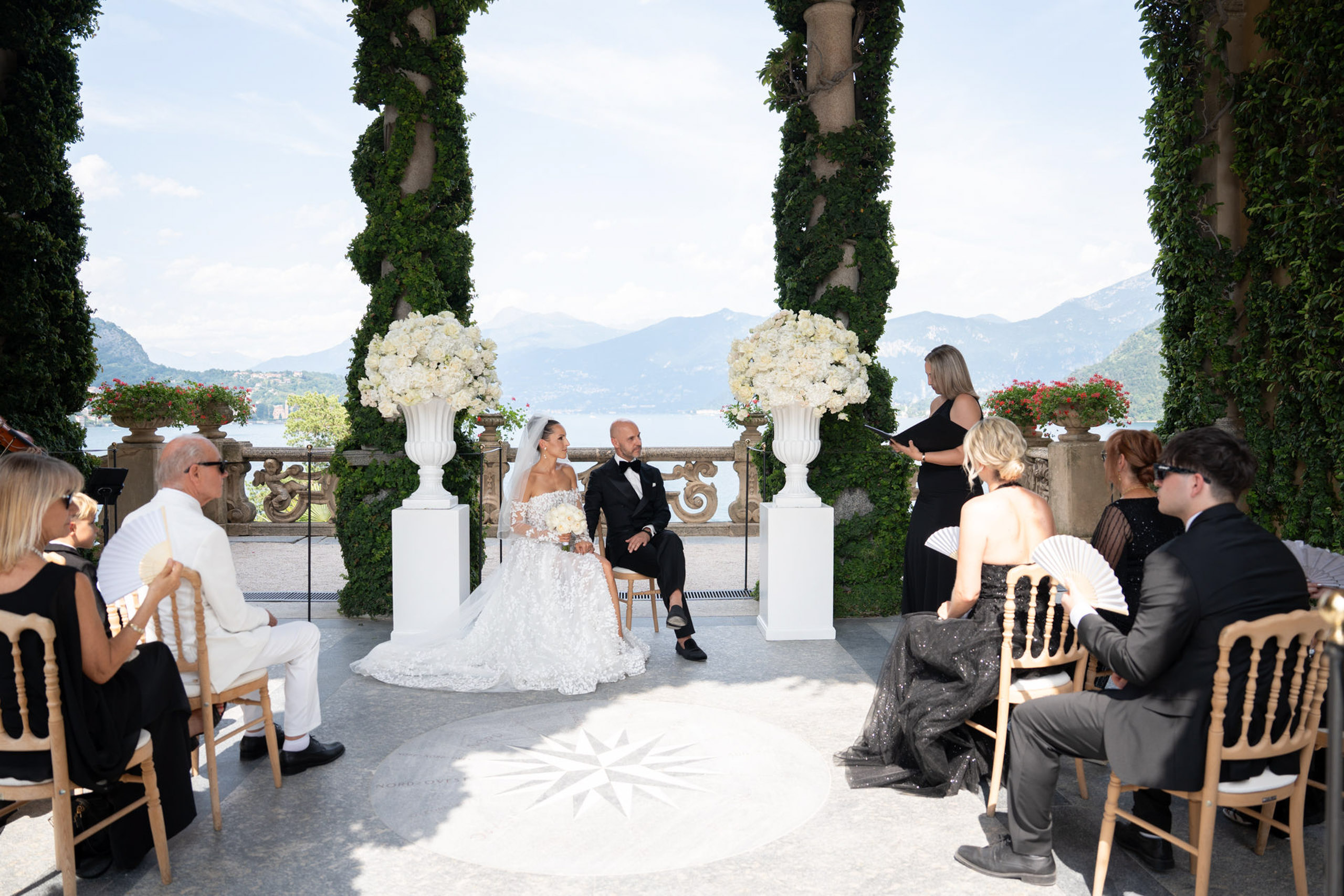 Villa del Balbianello Hochzeit: Kosten, Ablauf und die ikonischste Location am Comer See 21 A couple is sitting at the altar of Villa del Balbianello overlooking a lake.
