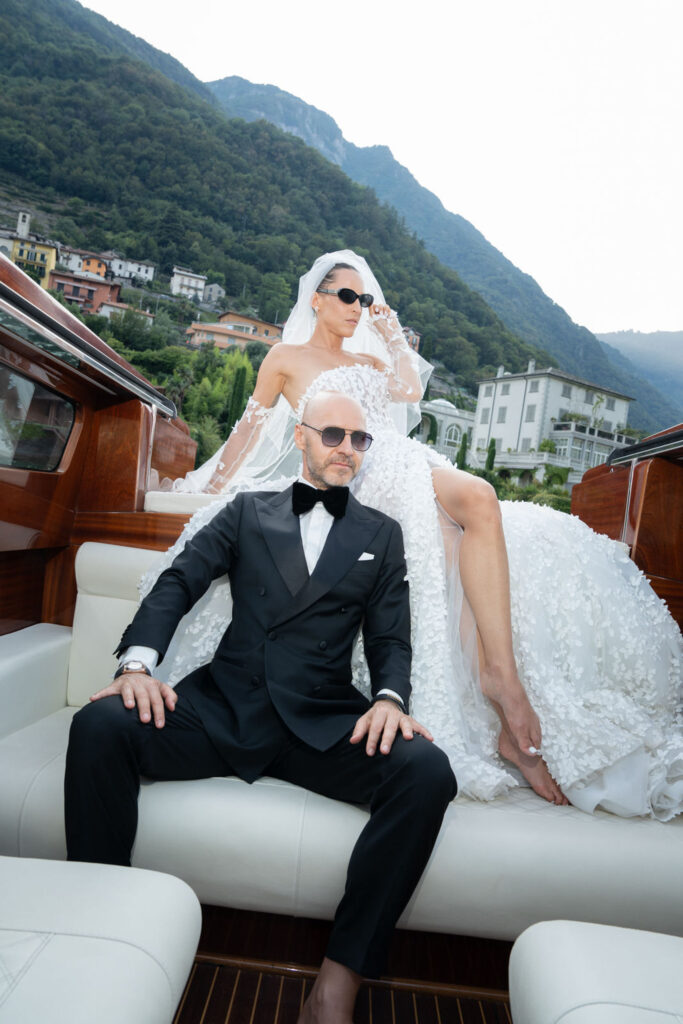 A bride and a man in a tuxedo are sitting together on a boat in Villa del Balbianello.
