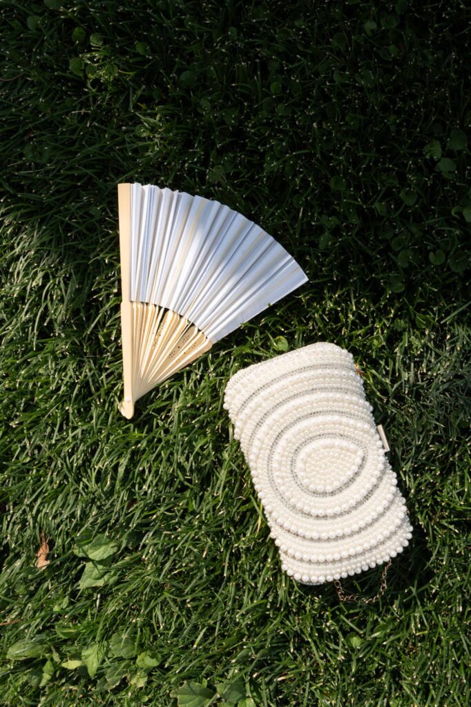Villa del Balbianello Hochzeit: Kosten, Ablauf und die ikonischste Location am Comer See 52 A white hand fan and a clutch adorned with pearls on the lawn of Villa del Balbianello.