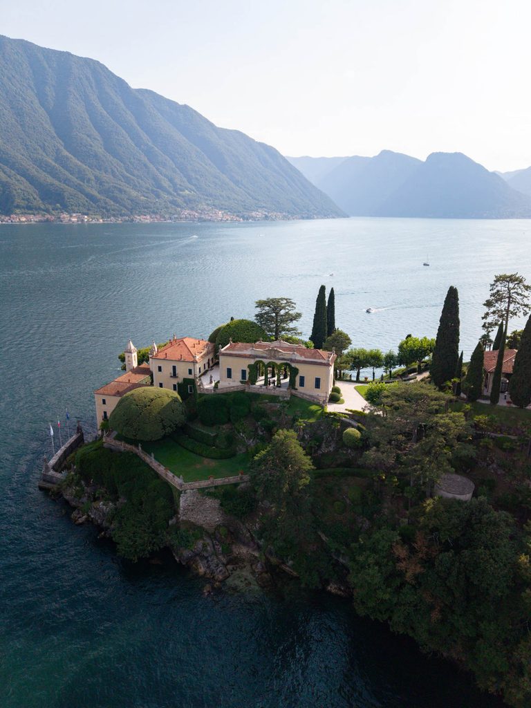Aerial view of Villa del Balbianello on a peninsula in Lake Como, surrounded by mountains.