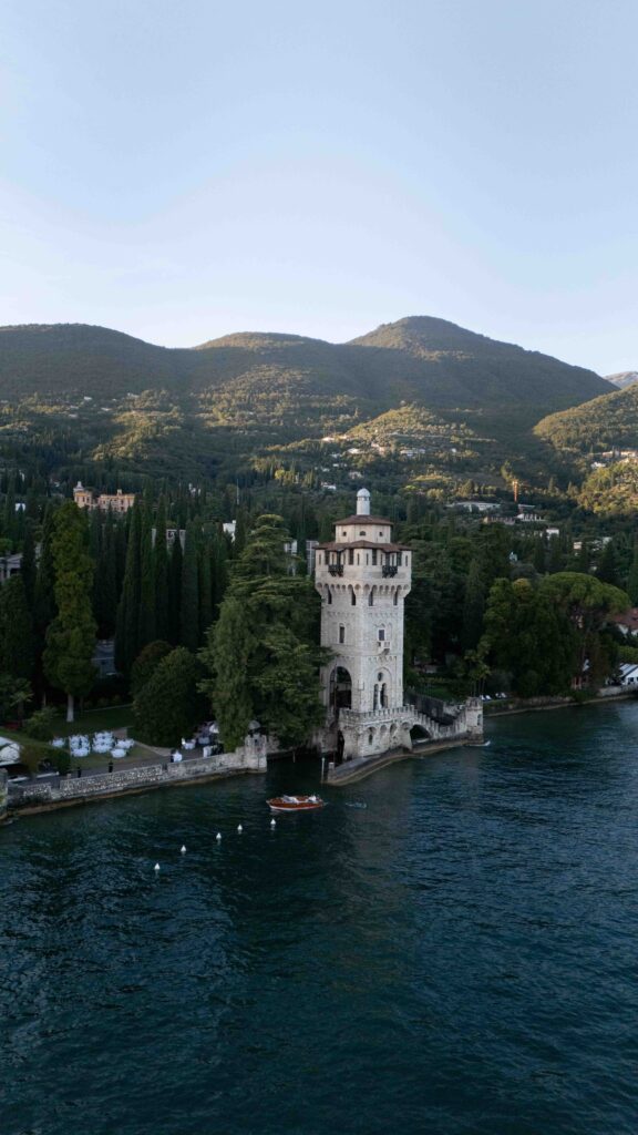 Steinturm am Seeufer, umgeben von Bäumen und Bergen unter klarem Himmel - ein bezaubernder Ort, der sich perfekt für die Auslandshochzeit oder zeitlose Hochzeitsfotografie-Momente eignet.