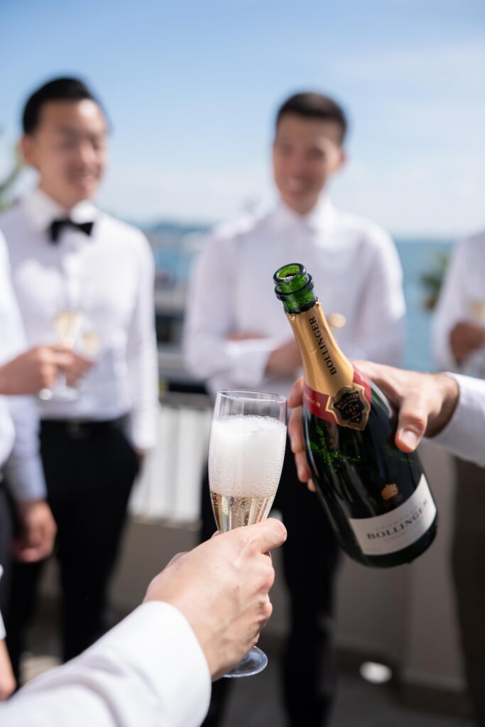Eine Person schenkt bei einem Treffen im Freien mit formell gekleideten Menschen Champagner in ein Glas ein und fängt damit die Eleganz der Hochzeitsfotografie im Ausland ein.