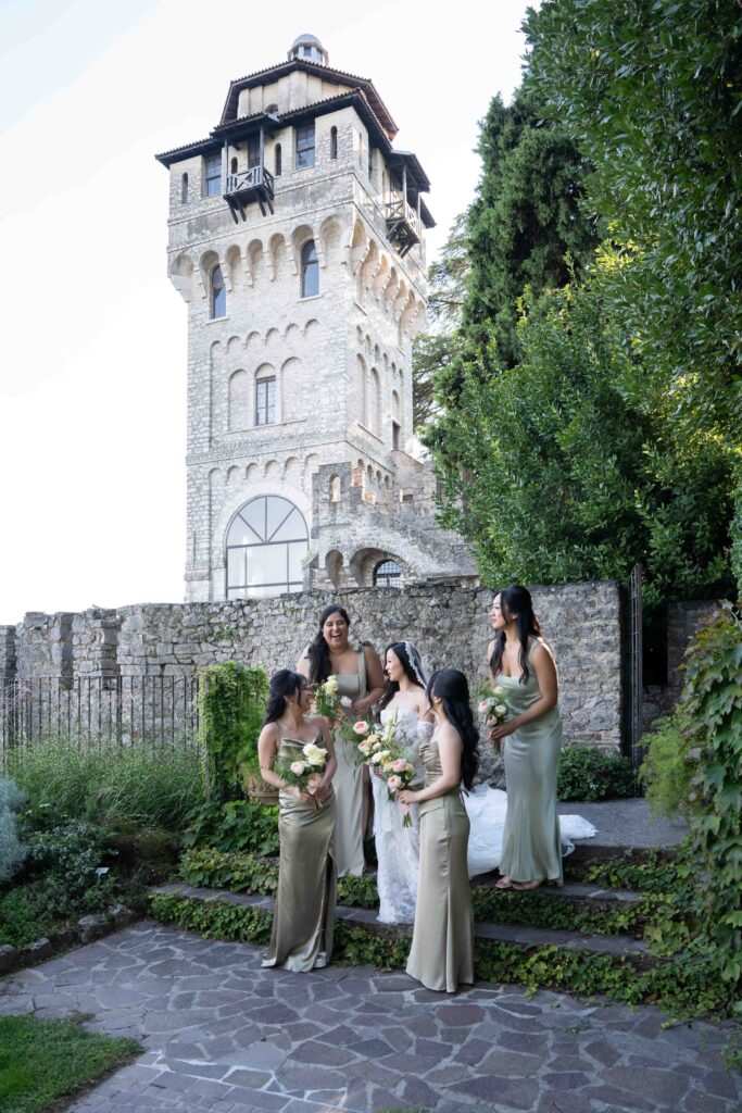 Eine Braut und Brautjungfern in hellen Kleidern stehen gemeinsam vor einem Steinturm im Grünen - ein perfekter Moment für Hochzeitsfotografie im Ausland.