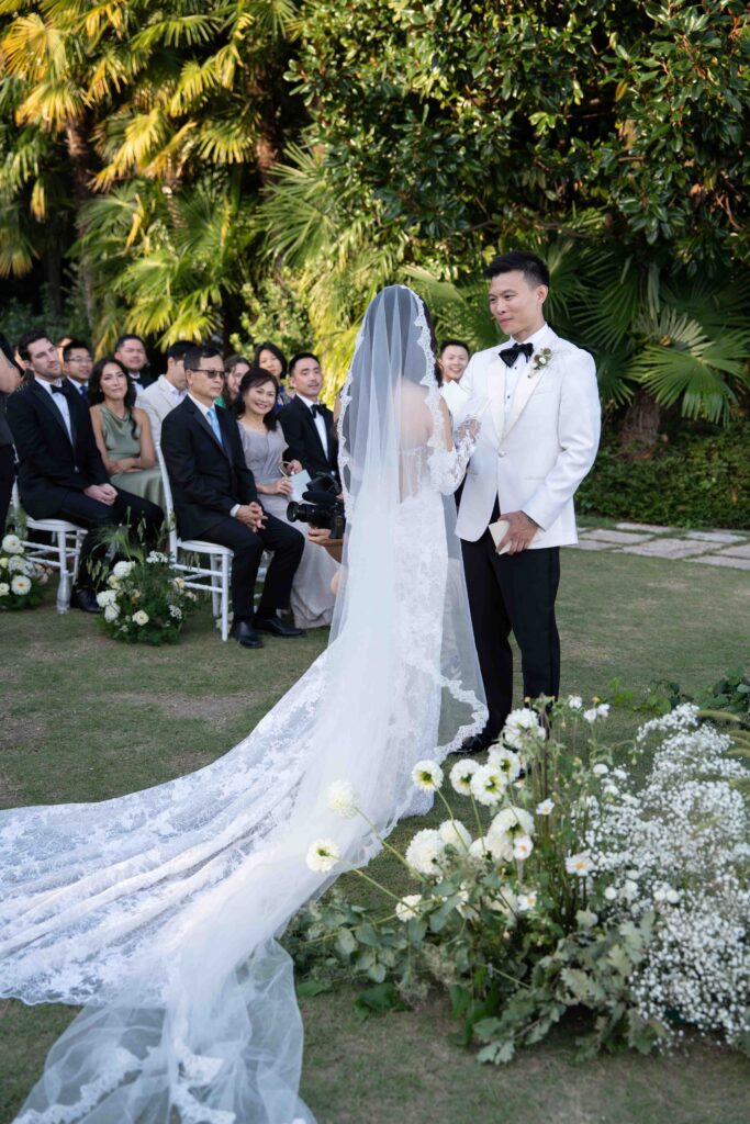 Braut und Bräutigam stehen während ihrer Trauung im Freien zusammen, umgeben von Gästen und Grün - ein perfekter Moment für Hochzeitsfotografin, die sich auf Destination Weddings spezialisiert hat.