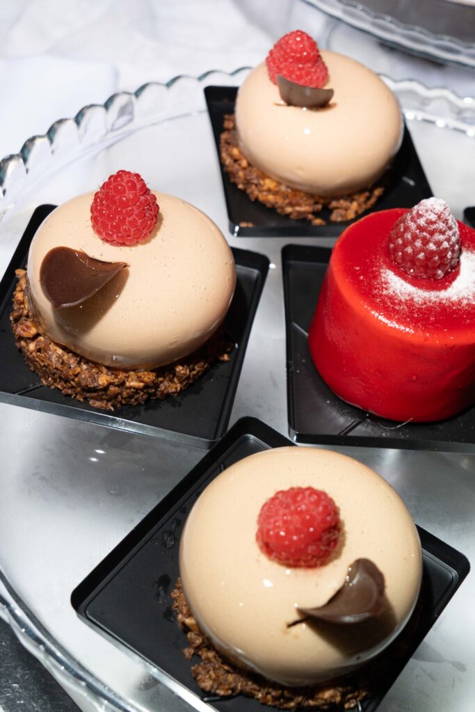 Vier elegante Desserts: drei runde Mousse-Torten mit Himbeeren und Schokoladendekor und eine rote Mousse-Torte - die perfekte süße Note für eine Hochzeitsfotografin, die unvergessliche Momente festhält.