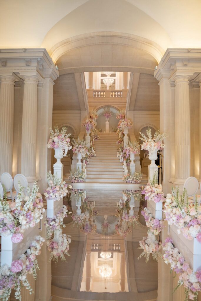 Eine prächtige Marmortreppe, geschmückt mit rosa und weißen Blumen, spiegelte sich auf dem glänzenden Boden wider – wie ein automatisch gespeicherter Entwurf von Eleganz und Charme.
