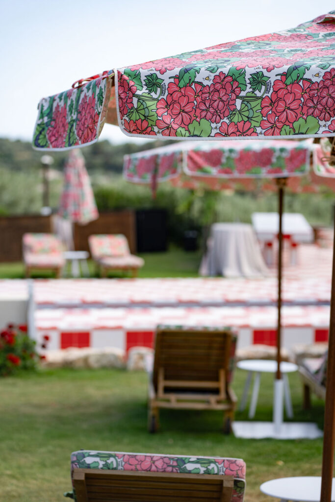 Regenschirme mit Blumenmuster und Liegestühle am Pool auf einer grasbewachsenen Wiese versprühen den entspannten Charme Italiens und erinnern an sonnenverwöhnte Tage in Sizilien, wobei ein sanft unscharfer Hintergrund die idyllische Szene noch unterstreicht.