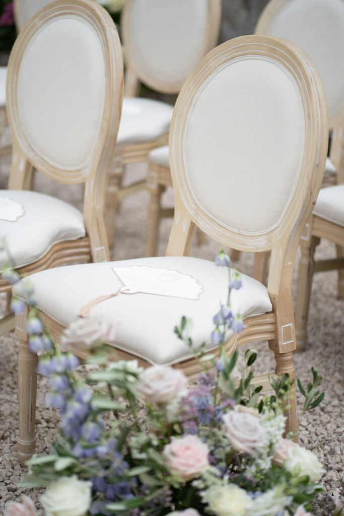 Elegante weiße Stühle mit Holzgestellen, die im Außenbereich von Stella Rheni aufgestellt sind, mit pastellfarbenen Blumen im Vordergrund – eine idyllische Kulisse für Ihre Hochzeit in Bonn oder zum Heiraten in Bonn.