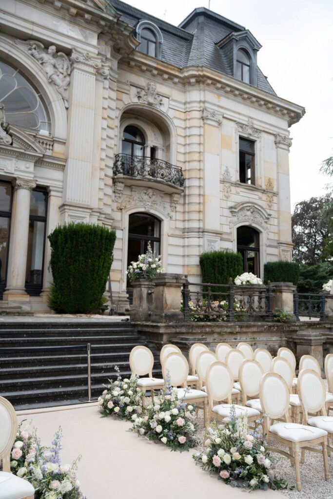 Elegante Hochzeitsdekoration im Freien mit weißen Stühlen und Blumenschmuck vor dem prächtigen historischen Gebäude „Stella Rheni“ – ein perfekter Rahmen für Ihre Hochzeit und zum Heiraten in Bonn.