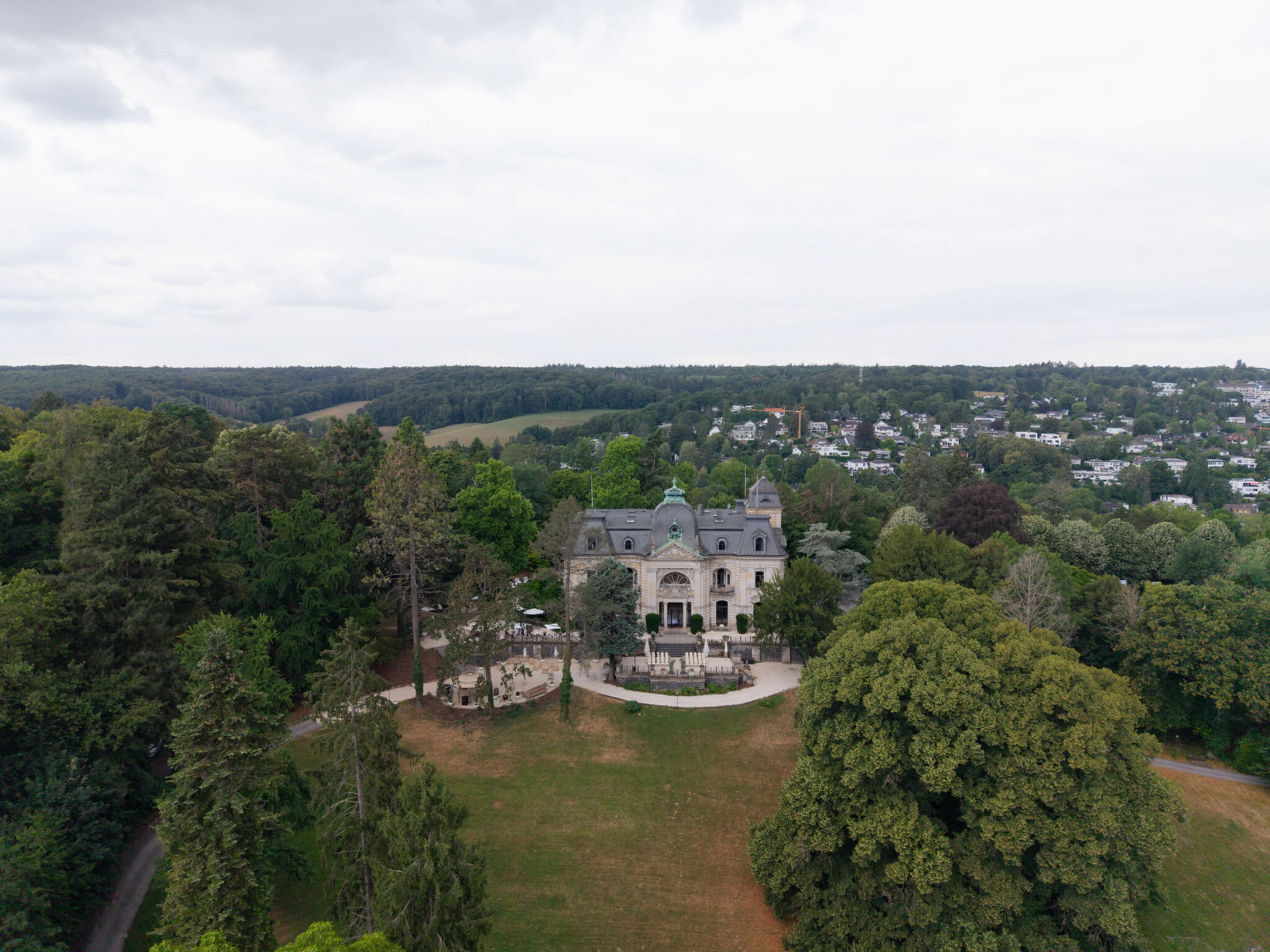 Luftaufnahme des historischen Herrenhauses „Stella Rheni“, umgeben von Bäumen und einer üppig grünen Landschaft unter bewölktem Himmel – eine ideale Kulisse für eine Hochzeit in Bonn oder für alle, die in Bonn heiraten möchten.