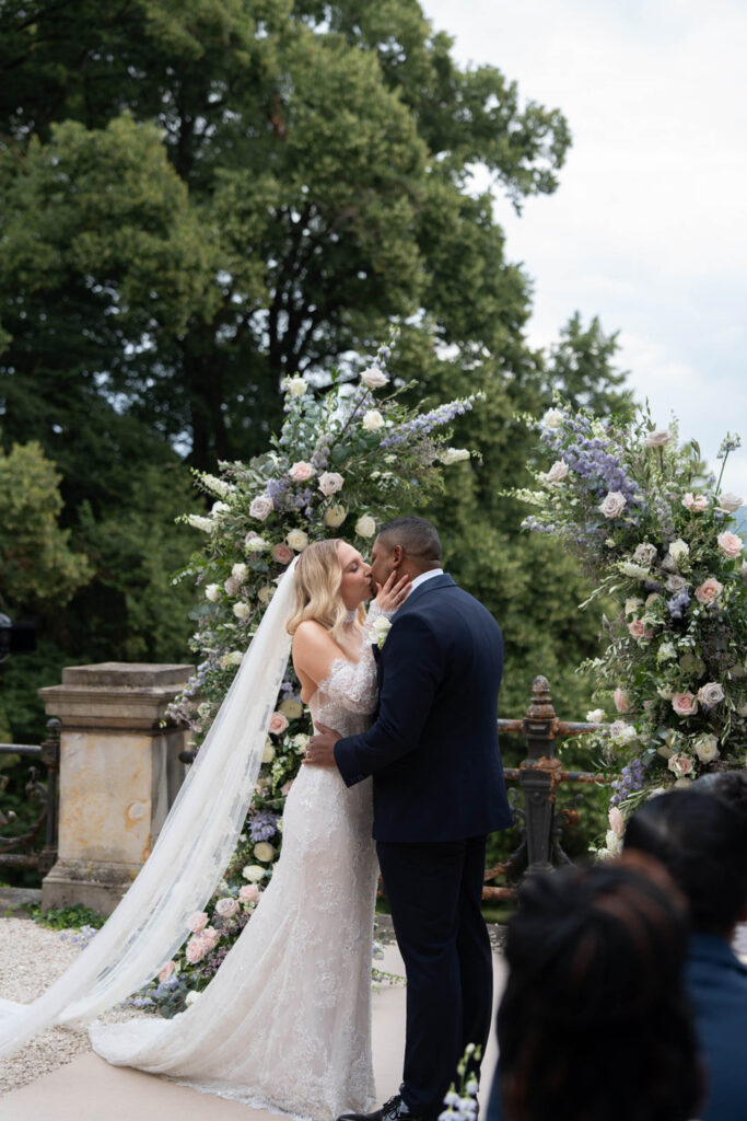 Braut und Bräutigam küssen sich bei ihrer Hochzeit im Freien im Stella Rheni, umgeben von Blumenbögen – ein unvergesslicher Moment für alle, die davon träumen, in Bonn zu heiraten.