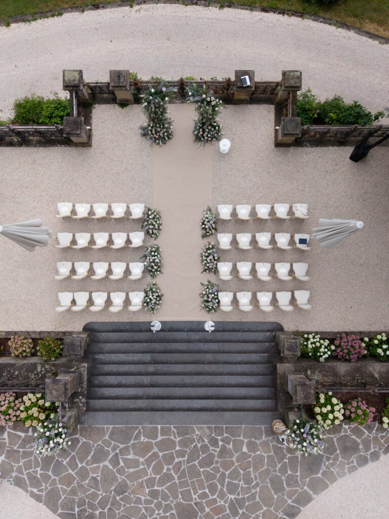 Luftaufnahme einer Hochzeitszeremonie im Freien mit weißen Stühlen und Blumenschmuck im Gang bei Stella Rheni – der perfekte Ort für eine Hochzeit in Bonn und für Paare, die davon träumen, in Bonn in einem eleganten Rahmen zu heiraten.