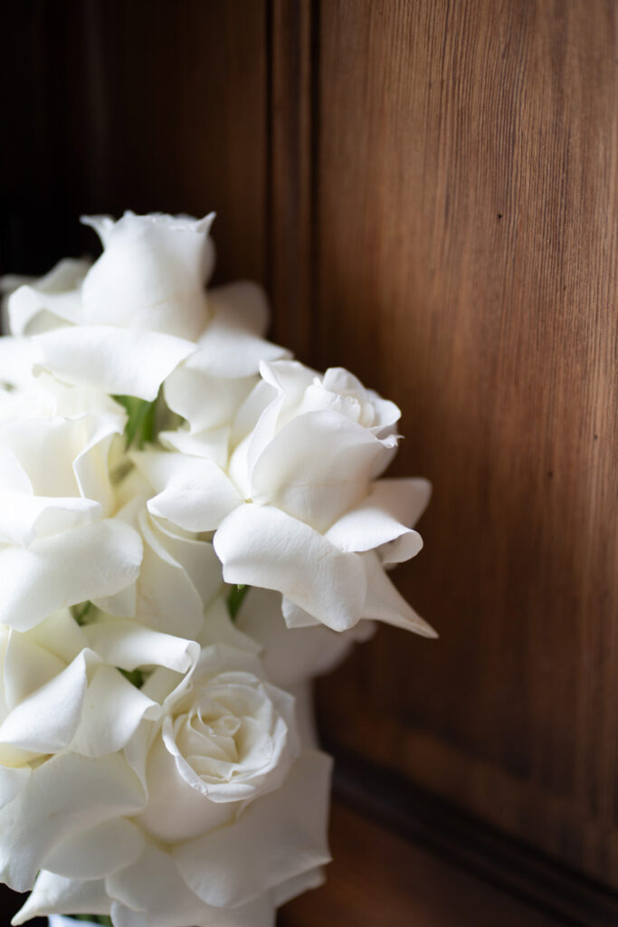Ein Strauß weißer Rosen ist vor einem hölzernen Hintergrund arrangiert und schafft so eine elegante Kulisse, die sich perfekt für eine Hochzeit in Bonn im wunderschönen Stella Rheni eignet.