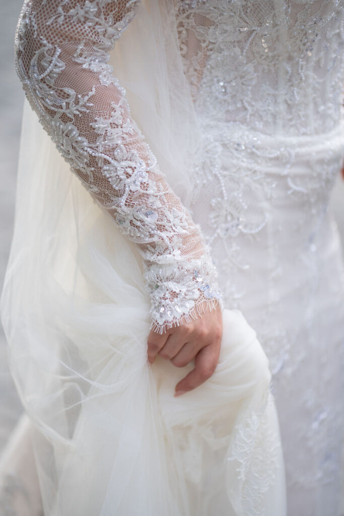 Nahaufnahme einer Person, die ein weißes Spitzenhochzeitskleid mit zarten Stickereien und Perlenverzierungen in der Hand hält – perfekt für eine „Stella Rheni Hochzeit Bonn“.
