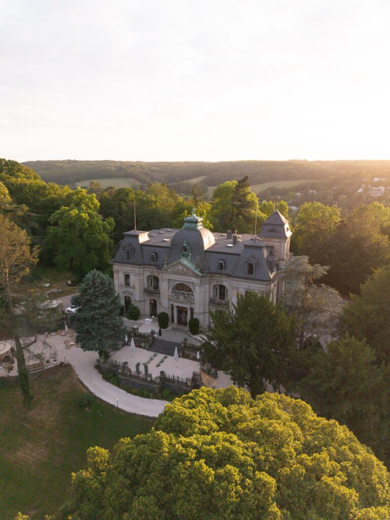 Luftaufnahme des prächtigen, historischen Herrenhauses Stella Rheni, umgeben von Bäumen und in warmes Sonnenlicht getaucht – eine wahrhaft bezaubernde Kulisse für eine Hochzeit oder zum Heiraten in Bonn.