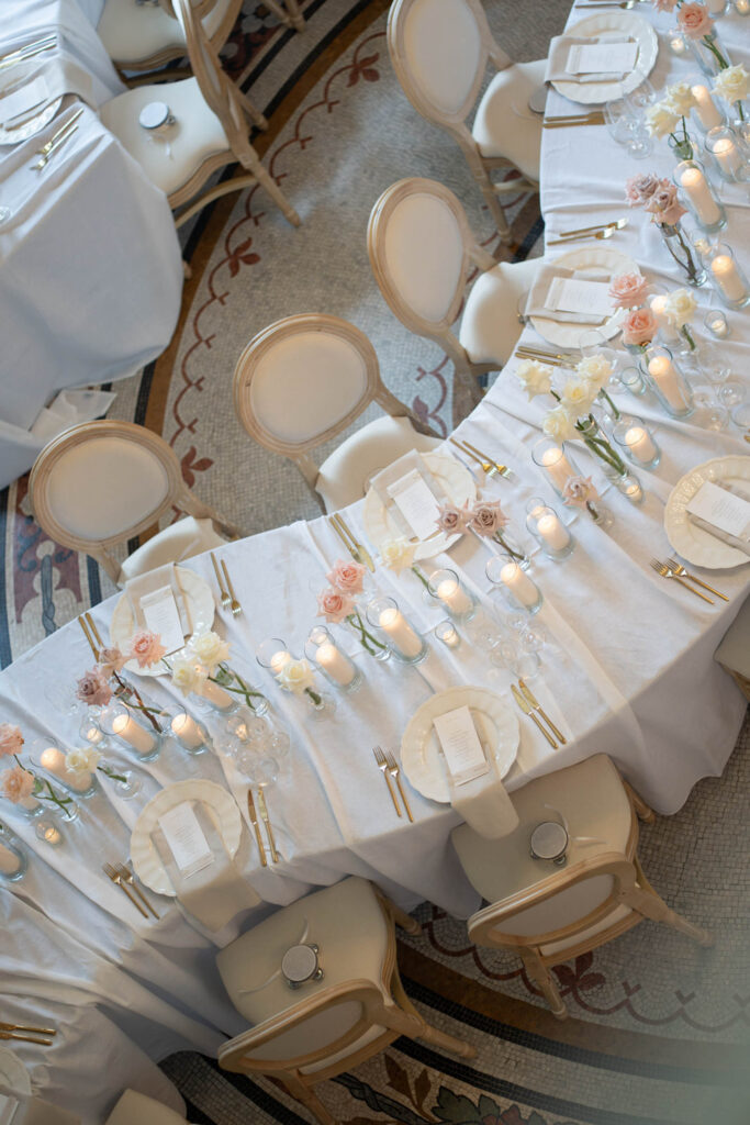 Ein geschwungener Banketttisch mit weißem Tischtuch, Kerzen, pastellfarbenen Blumen, Tellern und eleganten Stühlen, gedeckt für eine Veranstaltung im Stella Rheni – perfekt für eine Hochzeit in Bonn oder alle, die in Bonn stilvoll heiraten möchten.