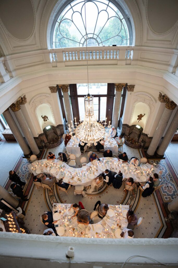 Ein elegantes Bankett in einem prächtigen Saal mit Kronleuchter, großen Fenstern und geschwungenen weißen Tischen, an denen sich die Gäste drängen – eine unvergessliche Hochzeit im Stella Rheni, der perfekte Rahmen für alle, die davon träumen, in Bonn zu heiraten.