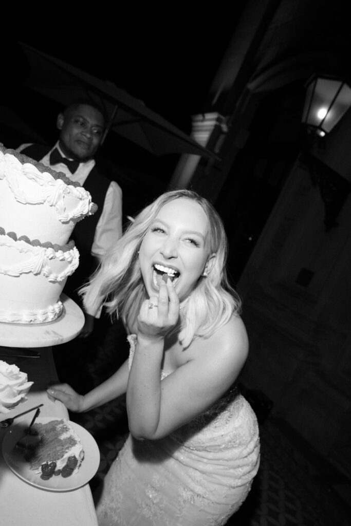 Eine strahlende Braut im Brautkleid genießt an ihrer Hochzeit ein Stück Torte, neben ihr stehen ein Kellner und eine große mehrstöckige Torte – die wunderschöne Feier findet im eleganten „Stella Rheni“ statt und macht das Heiraten in Bonn zu einem wahrhaft unvergesslichen Erlebnis.