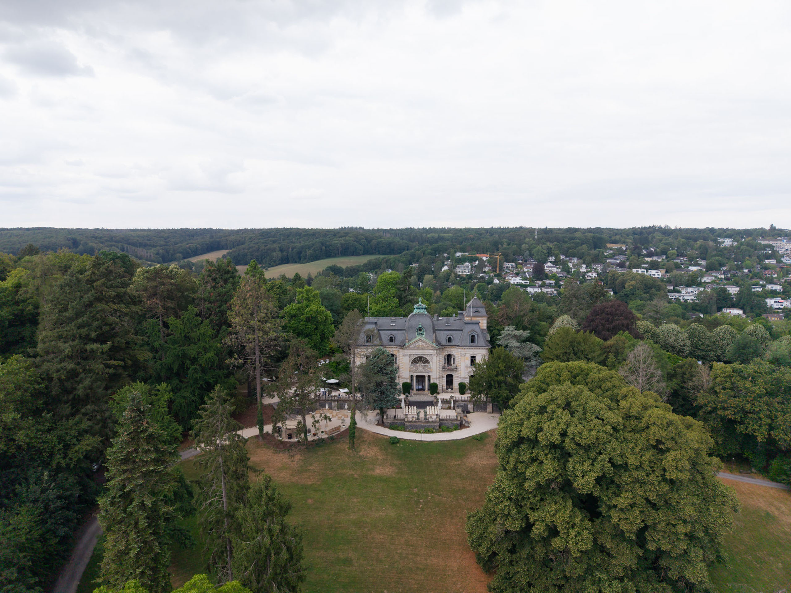 Luftaufnahme des historischen Herrenhauses „Stella Rheni“, umgeben von Bäumen und einer üppig grünen Landschaft unter bewölktem Himmel – eine ideale Kulisse für eine Hochzeit in Bonn oder für alle, die in Bonn heiraten möchten.