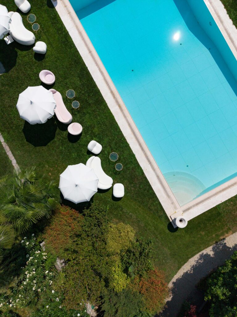 Aerial view of a pool with white umbrellas, sun loungers and a garden with green grass – an elegant backdrop that is perfect for wedding photos.