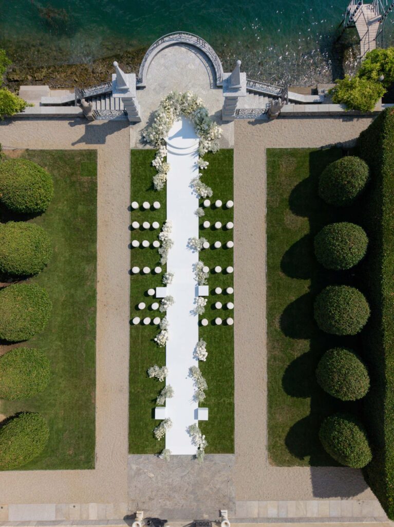 Luftaufnahme eines Hochzeitsgangs im Freien mit weißen Stühlen, Blumenschmuck und gepflegten Gärten in der atemberaubenden Villa Balbiano am Comer See – eine idyllische Kulisse, um in zeitloser Eleganz zu heiraten.