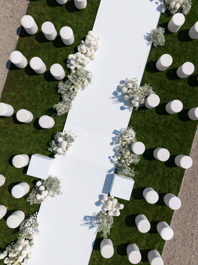 Ein weißer Gang mit Blumenschmuck, umgeben von runden weißen Stühlen auf grünem Rasen, von oben betrachtet – eine bezaubernde Kulisse, perfekt für eine Hochzeit in der prächtigen Villa Balbiano am Ufer des Comer Sees.