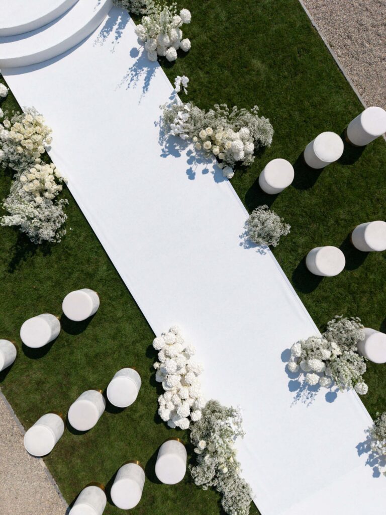 Ein weißer Gang mit runden Hockern und weißen Blumenarrangements auf grünem Rasen, von oben betrachtet – eine elegante Kulisse, die an die prächtigen Palazzi der Villa Balbiano erinnert und perfekt für Paare ist, die am Comer See heiraten möchten.